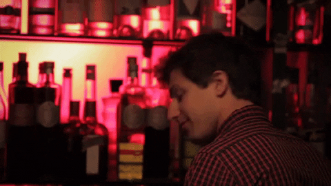Andy Samberg is a smiling bartender in a low-lit bar in Portlandia (gif).