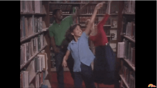Levar Burton and two women dance excitedly in a library from Reading Rainbow. [gif]
