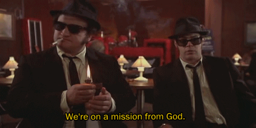 Elwood Blues (played by Dan Ackroyd) says, "We're on a Mission from God" as Jake Blues (played by John Belushi) smokes and flicks his lighter. [gif from The Blues Brothers, 1980]