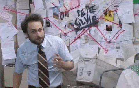 Charlie from It's Always Sunny smokes a cigarette, stressed out, as he tries to connect the dots in a Beautiful Mind-style wall of conspiracy theories.